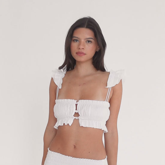 Video of model wearing the Eran Top in white, showing the ruffled straps, button-front closure, and lightweight cotton fabric while she turns and poses to display the fit and details**white