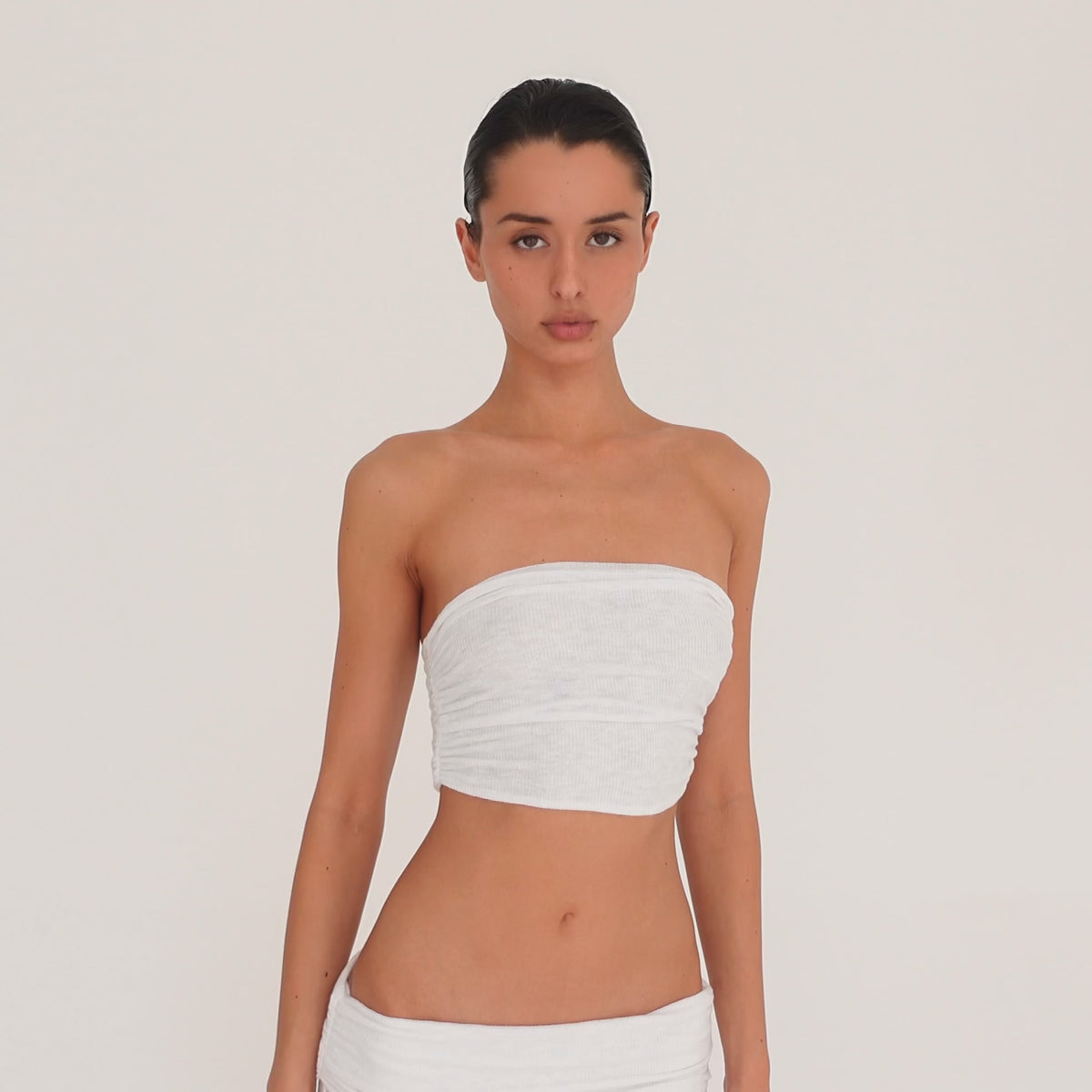 Video: Model turns and poses in the Meili Bandeau in White, showing the cropped strapless fit, all-over ruching and fitted silhouette from multiple angles. **white