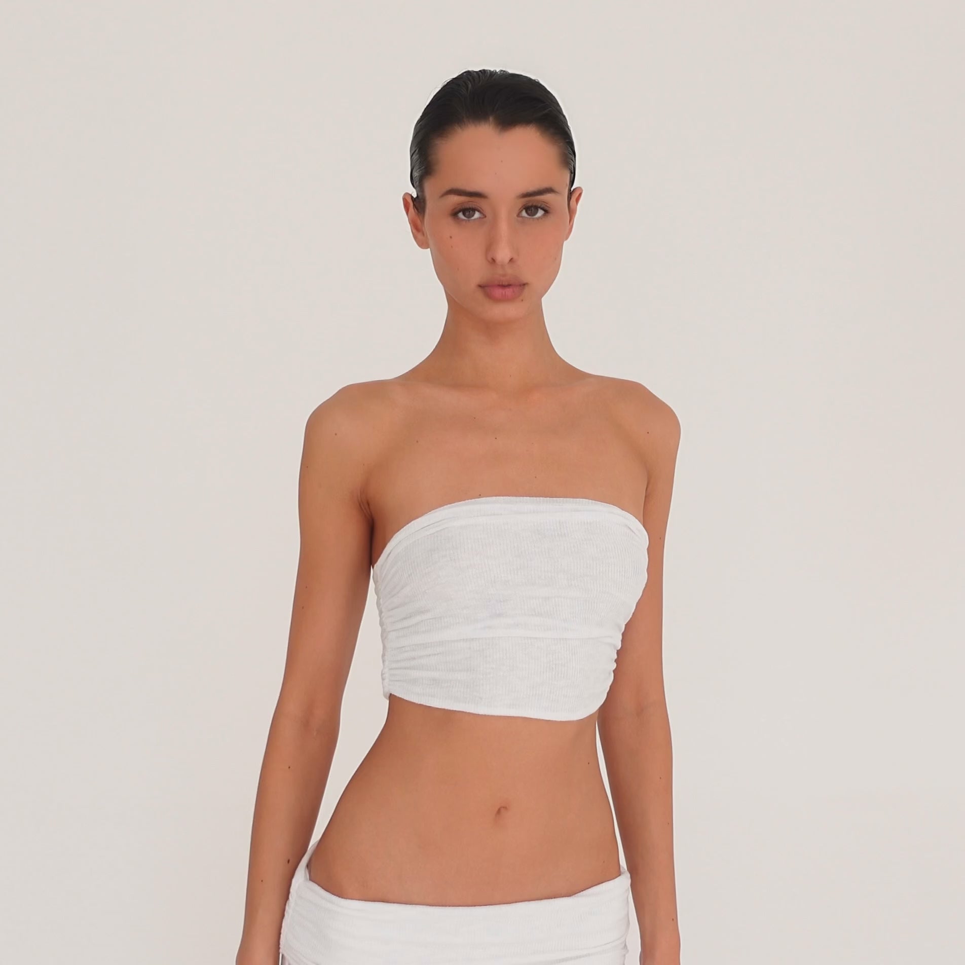 Video: Model turns and poses in the Meili Bandeau in White, showing the cropped strapless fit, all-over ruching and fitted silhouette from multiple angles. **white