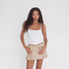 Video showing model walking and lightly swaying side to side while wearing the sand corduroy mini skirt with ribbed waistband, demonstrating skirt’s pleated structure, soft texture, and flattering low-rise fit. **sand