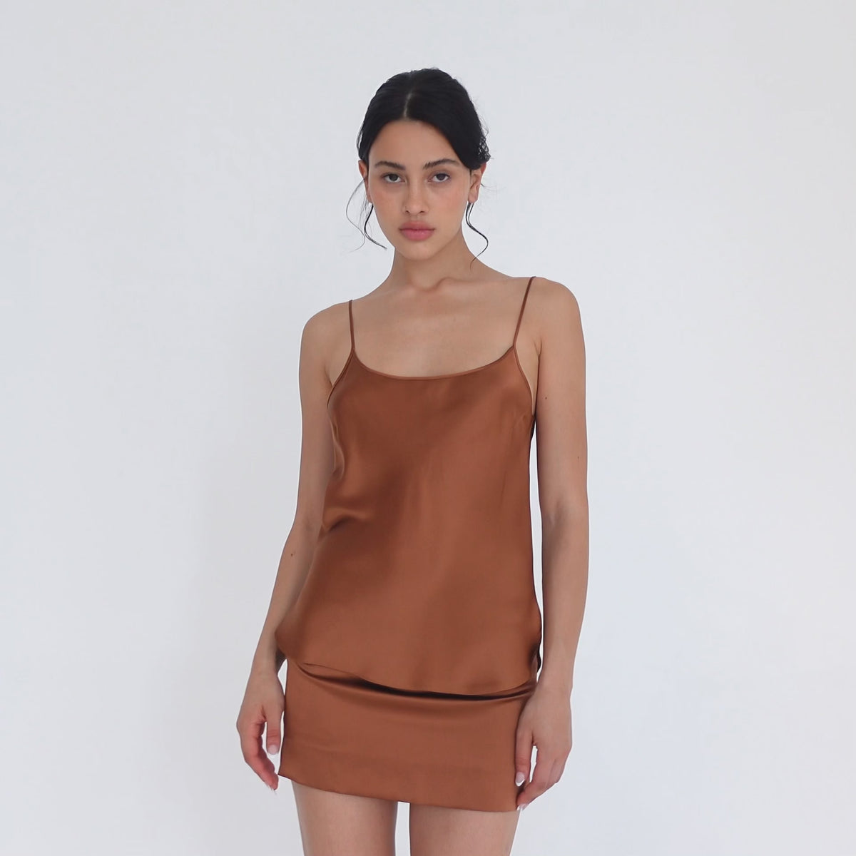 Model turning slowly in the copper silk Tini Skirt, showing the straight mini fit from the front, side and back, and the small side slit at the hem. **copper
