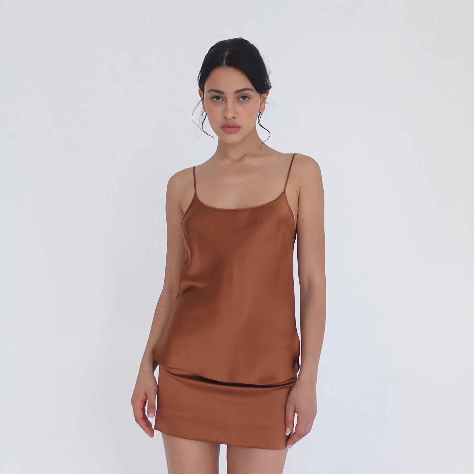 Model turning slowly in the copper silk Tini Skirt, showing the straight mini fit from the front, side and back, and the small side slit at the hem. **copper