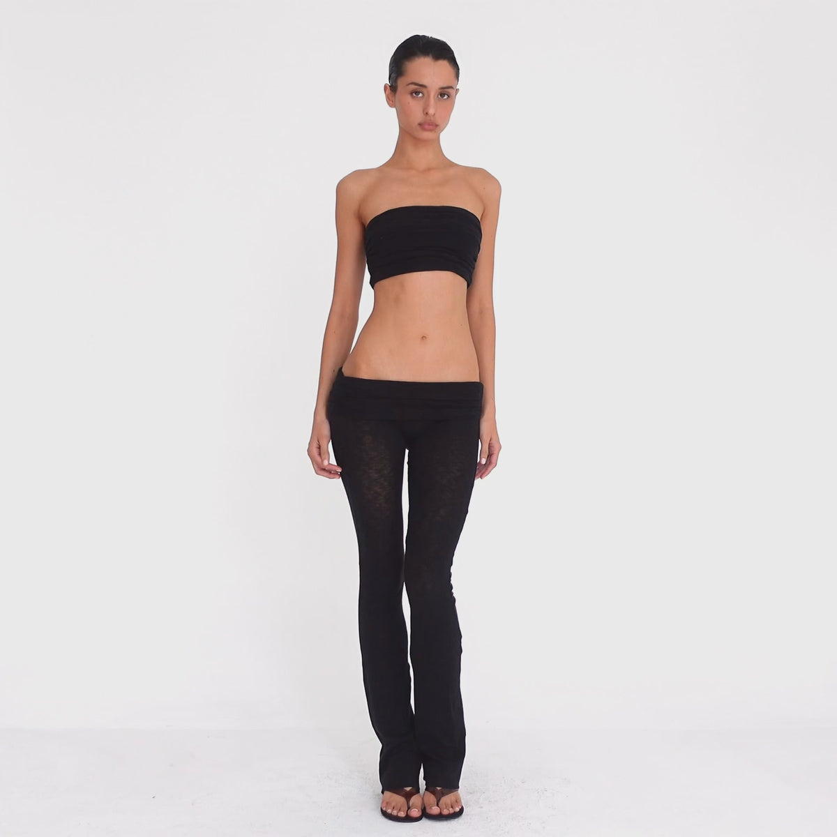 Model turns and poses in the Meili Pant in Black, showing the ultra low rise fit, wide ruched fold-over waistband, sheer fabric and subtly flared leg. **black