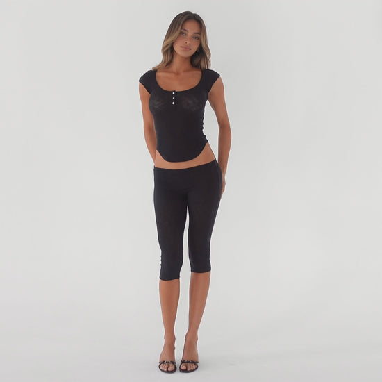 Video showing a model wearing a fitted cap sleeve henley top and capri leggings, highlighting the stretch, sheerness, and movement of the lightweight baby rib fabric in motion **black