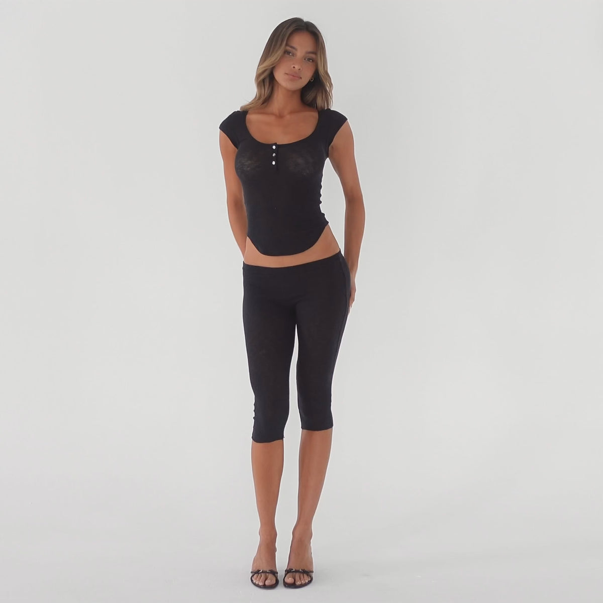 Video showing a model wearing a fitted cap sleeve henley top and capri leggings, highlighting the stretch, sheerness, and movement of the lightweight baby rib fabric in motion **black