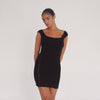 Model wearing the black Nikisa Dress — off-shoulder ribbed mini with gold hook-and-eye closures running down each side, hugging the body in a sculpted silhouette.**black