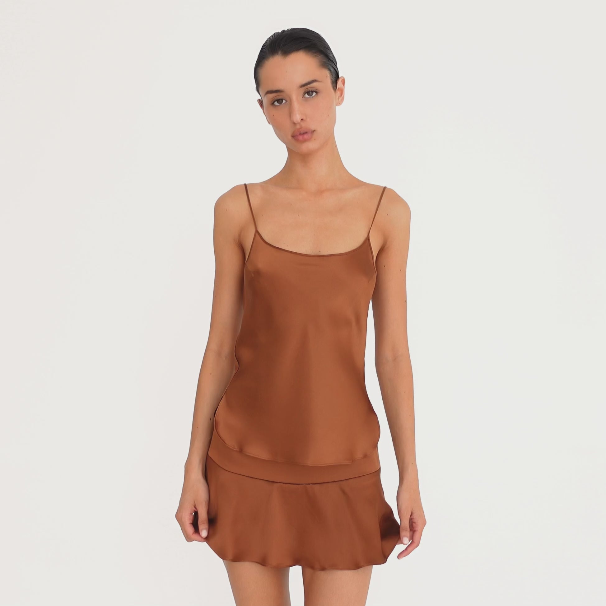 Video: Model wearing and moving in the Are You Am I Syra Skirt in Copper, showing the fluid drape and movement of the silk charmeuse mini skirt. **copper