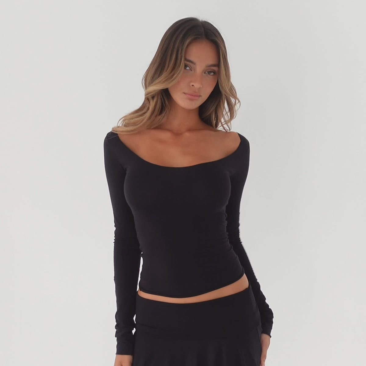 model moving and turning in a fitted off shoulder long sleeve top with a scoop neckline, showing the silhouette and stretch of the fabric **black