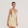Video: Model wearing the Atalanta Floral Dress in pale yellow, showing the plunging halter neckline, open back and sides, fitted silhouette, multicolor floral print, and layered ruffle mini hem from multiple angles.