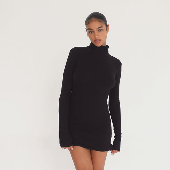 Video: Model wearing the ARE YOU AM I Denz Dress in black, moving and turning to show the fitted long-sleeve turtleneck silhouette and dramatic open back **black