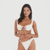 Video: Model moves and turns while wearing the Seren Swim Bottom in Cream with the Nou Swim Top, showing the textured fabric, high-cut fit, slim side straps, and front, side, and back views **cream