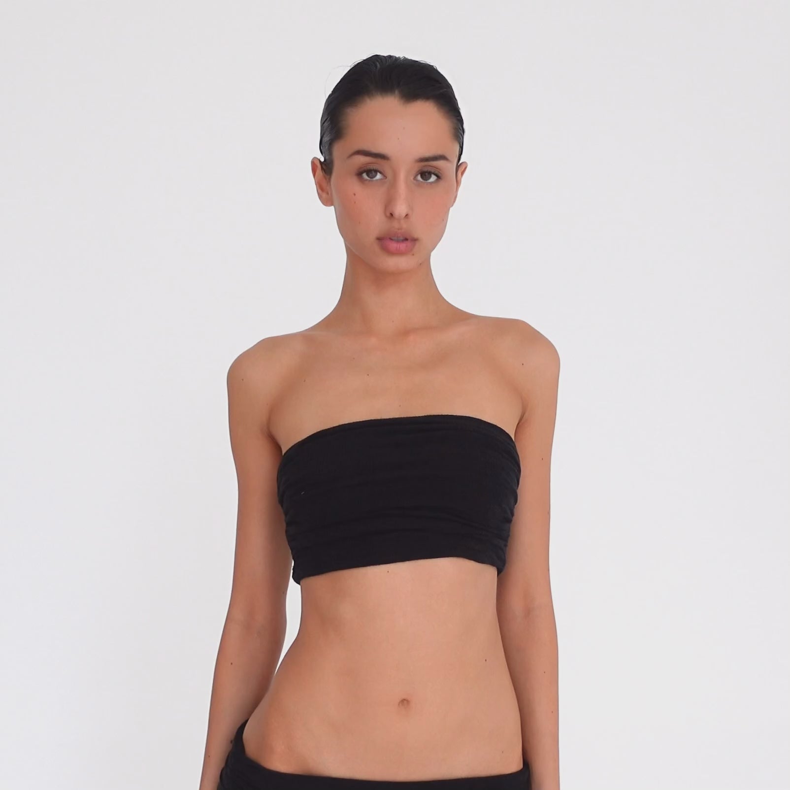 Video: Model turns and poses in the Meili Bandeau in Black, showing the cropped strapless fit, all-over ruching and fitted silhouette from multiple angles. **black