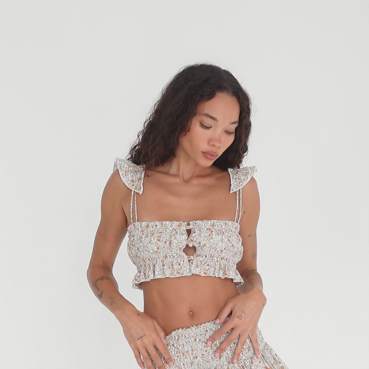 Model showcasing the Are You Am I Eran Top in floral, a smocked ruffle crop top with button front closures and frill straps, styled with the matching Eran Skirt, shown from multiple angles. **floral