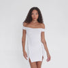 Video shows a model wearing the Nikisa Dress in white, featuring an off-the-shoulder neckline, gold hook-and-eye closures along the sides, and a fitted mini-length silhouette. **white
