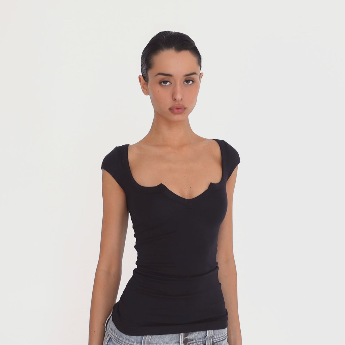 Video: Model moves to show the black Impy Tee from front, side and back angles, highlighting its close fit, cap sleeves and sculpted notched neckline. **black
