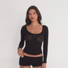Model wearing a sheer black long sleeve scoop neck cropped top with front buttons and matching fitted shorts, turning to show front and back views of the garment. **black