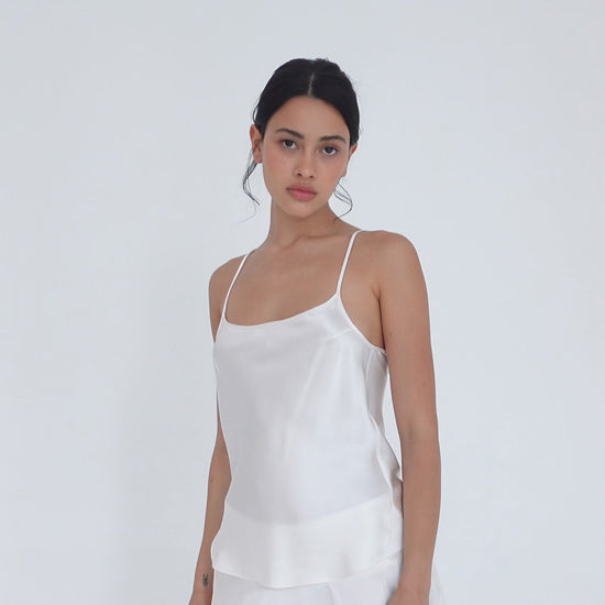 Model turning slowly in the white silk Syra Camisole, showing the scoop neckline from the front, the curved side hem and the low scoop back. **white