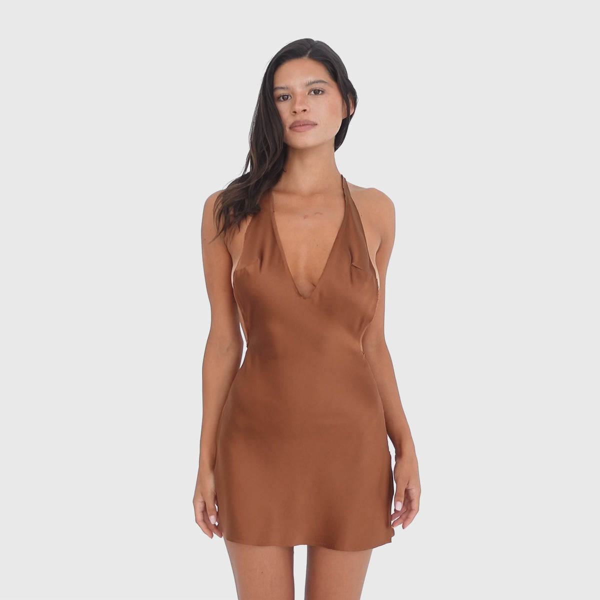 Video: Model moves and turns in the Atla Dress in Copper, showing the movement of the silk fabric and the dress’s plunging halter neckline, open sides, low open back, and fluid mini silhouette **copper