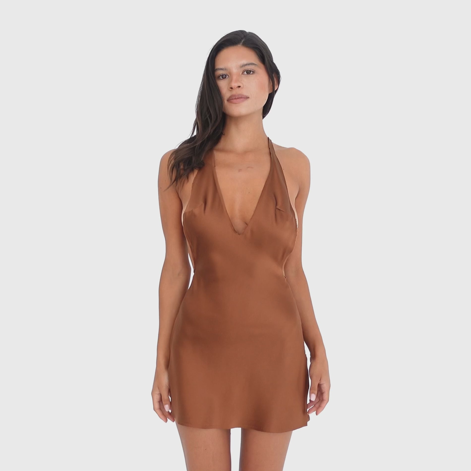Video: Model moves and turns in the Atla Dress in Copper, showing the movement of the silk fabric and the dress’s plunging halter neckline, open sides, low open back, and fluid mini silhouette **copper
