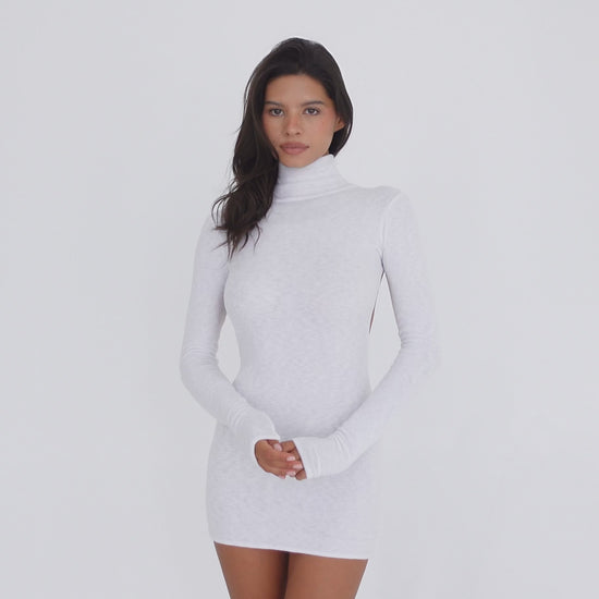 Video: Model wearing the ARE YOU AM I Denz Dress in white, turning to show the fitted long-sleeve turtleneck mini dress and dramatic open-back design **white