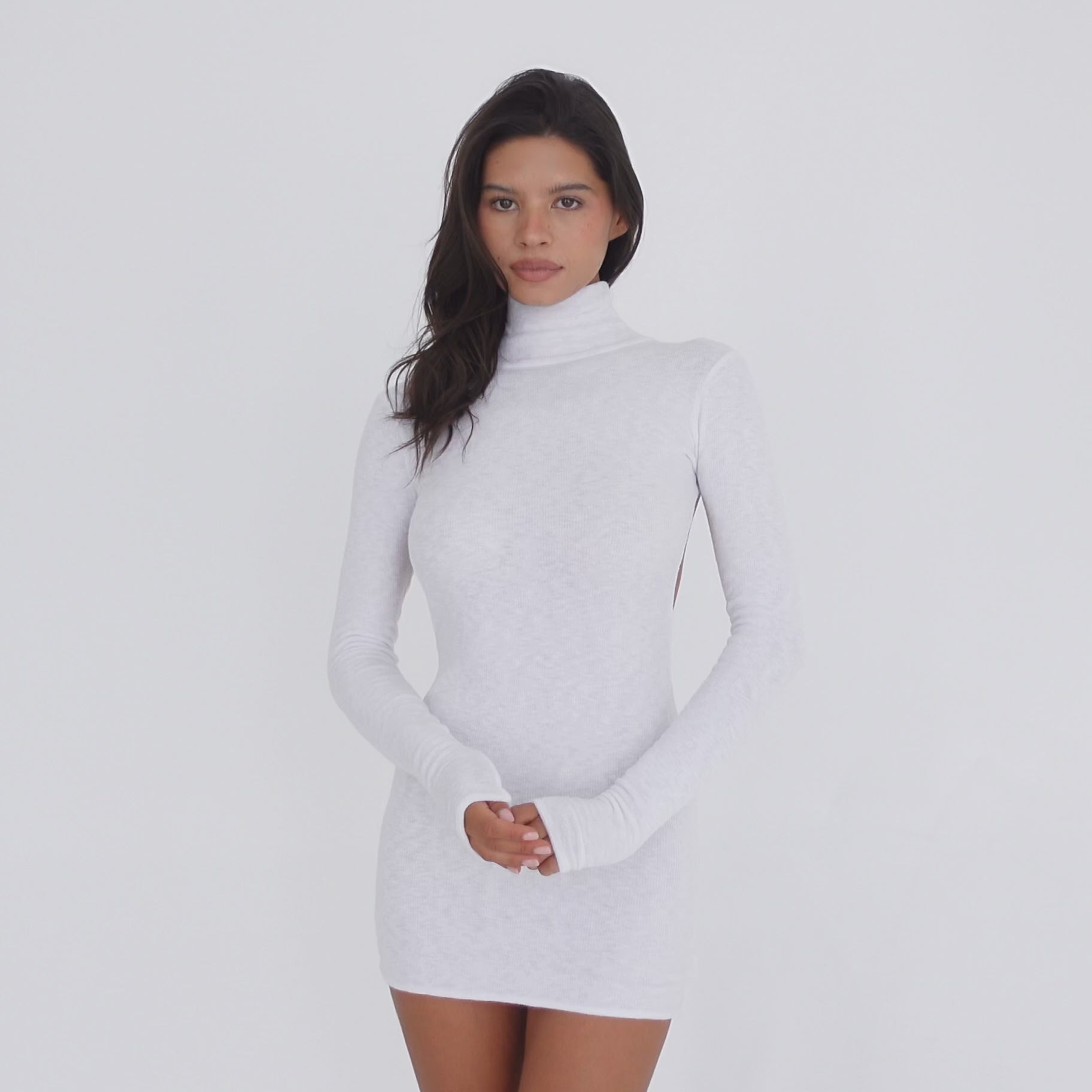 Video: Model wearing the ARE YOU AM I Denz Dress in white, turning to show the fitted long-sleeve turtleneck mini dress and dramatic open-back design **white