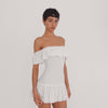 Model moves and poses in the white Zouette mini dress to show the off shoulder ruffled neckline, fitted smocked bodice, short pleated skirt, and overall silhouette from different angles