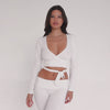 Video of a model wearing a white long-sleeve wrap crop top, showing front, side, and back views to highlight the wrap fit, deep V neckline, and stretchy active fabric **white