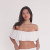 Model wearing a white off-the-shoulder ruffle bandeau and matching smocked mini skirt. The video shows front, side, and back angles, demonstrating the drape of the ruffle overlay and the fit of the smocked waistband.