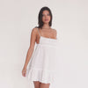 Model moving in a white cotton smocked mini dress with thin adjustable straps, gathered bust, fitted waist, and soft ruffle hem, shown from front, side, and back.